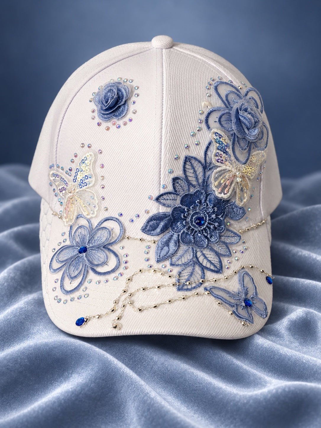 White statement cap with blue floral lace appliques, butterflies, rhinestones, and delicate chain accents